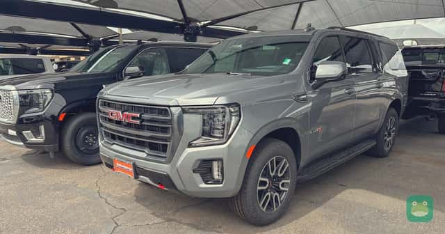 A new GMC Yukon SUV parked on a car dealership lot under hail protection awnings.